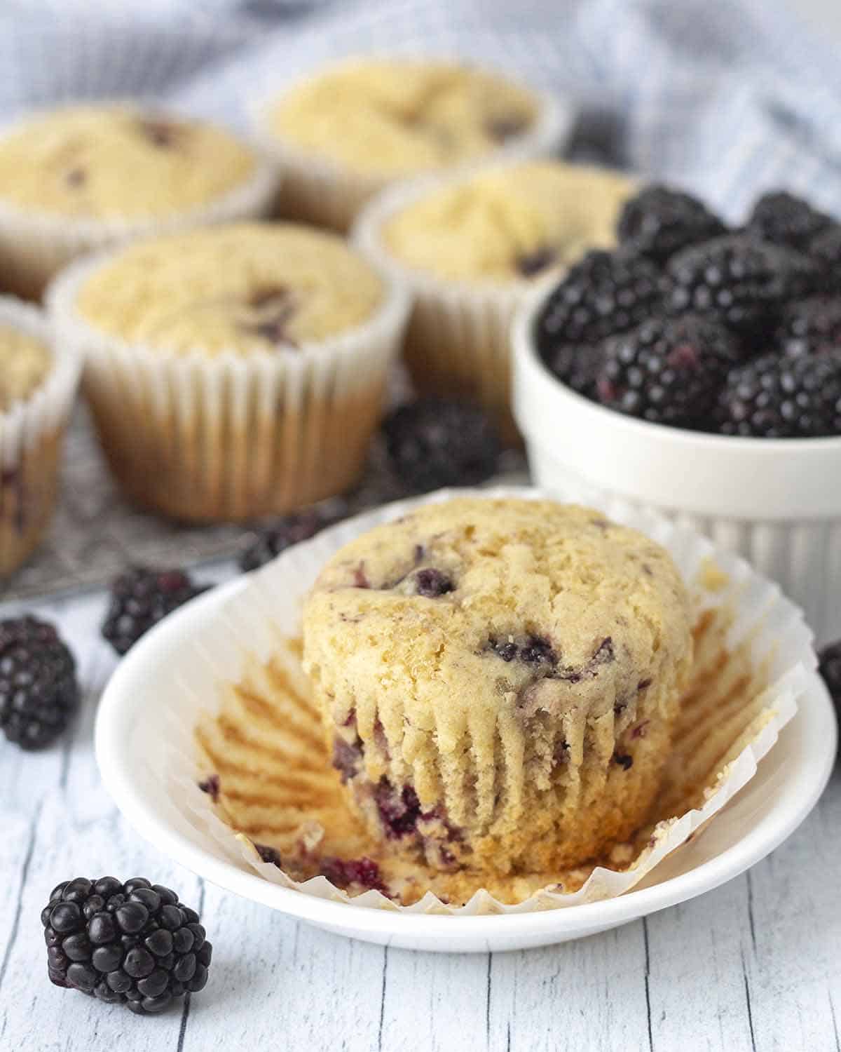 A blackberry muffin on a plate, the muffin wrapper has been peeled away to be removed.