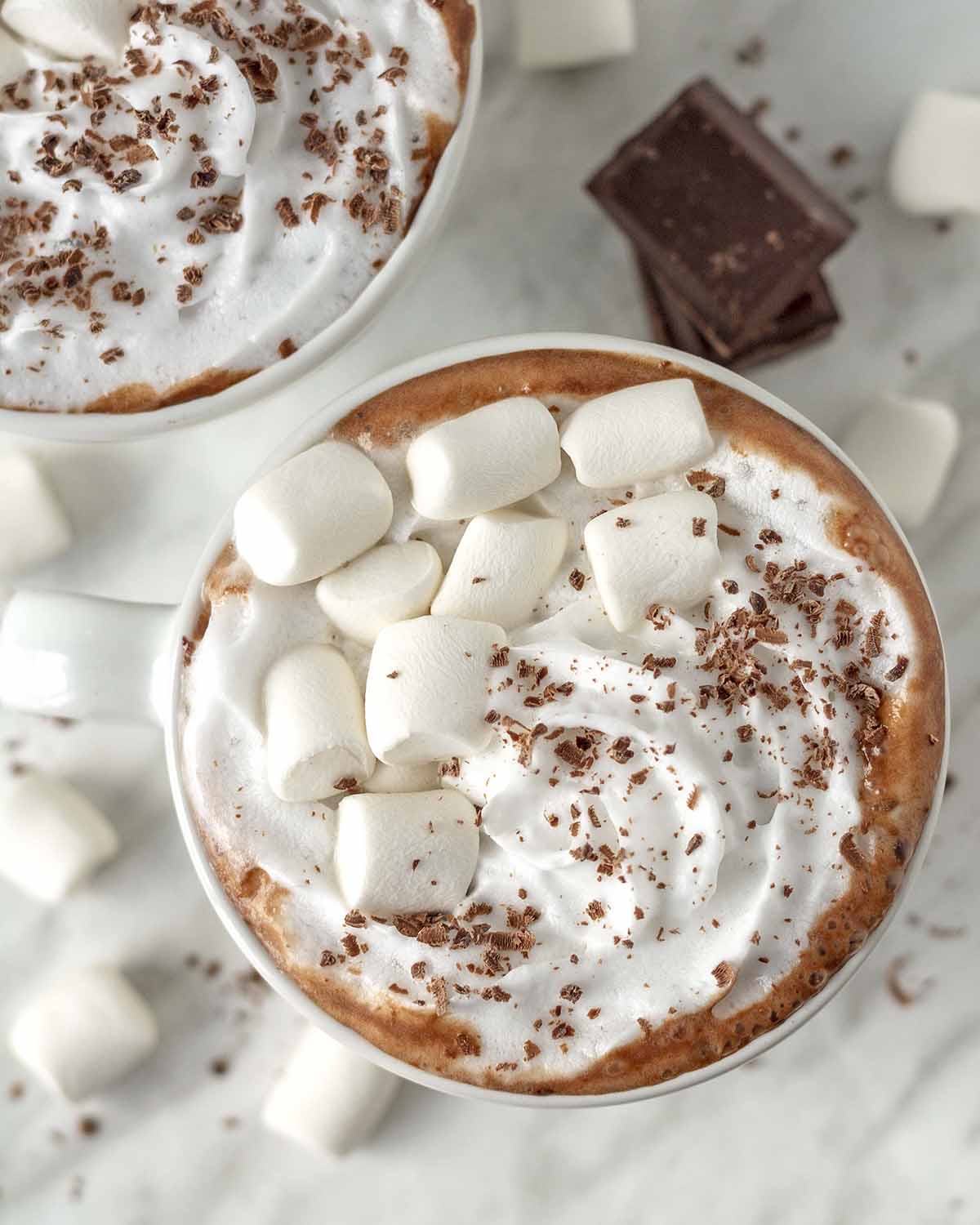 An overhead shot of oat milk hot chocolate in a white cup and garnished with vegan marshmallows and whip.