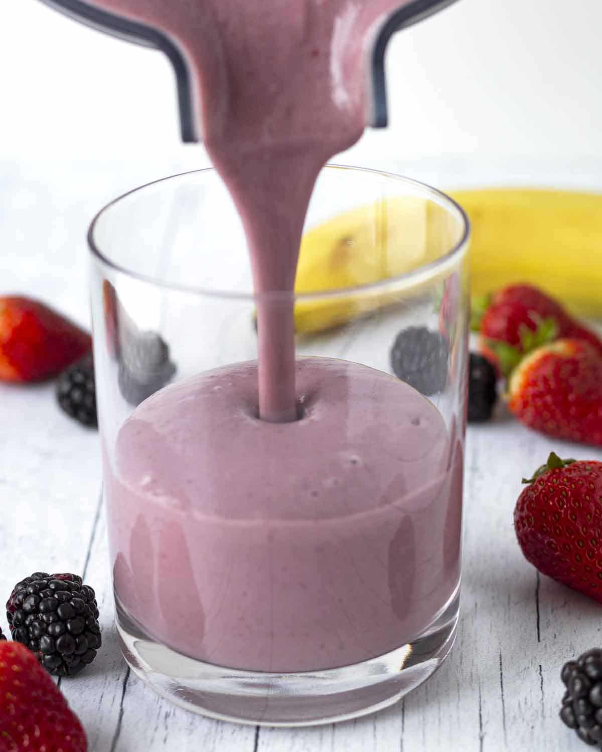 Freshly blended strawberry banana smoothie being poured from a blender container into a glass.