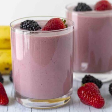 Two glasses filled with a bright coloured berry smoothie, fresh berries surround the glasses.