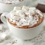 A cup full of dairy-free hot cocoa, it’s garnished with whipped cream, marshmallows, and chocolate.