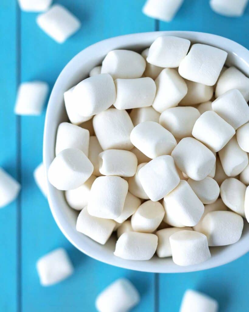 An overhead view showing marshmallows in a small white bowl, the bowl is surrounded by more marshmallows.
