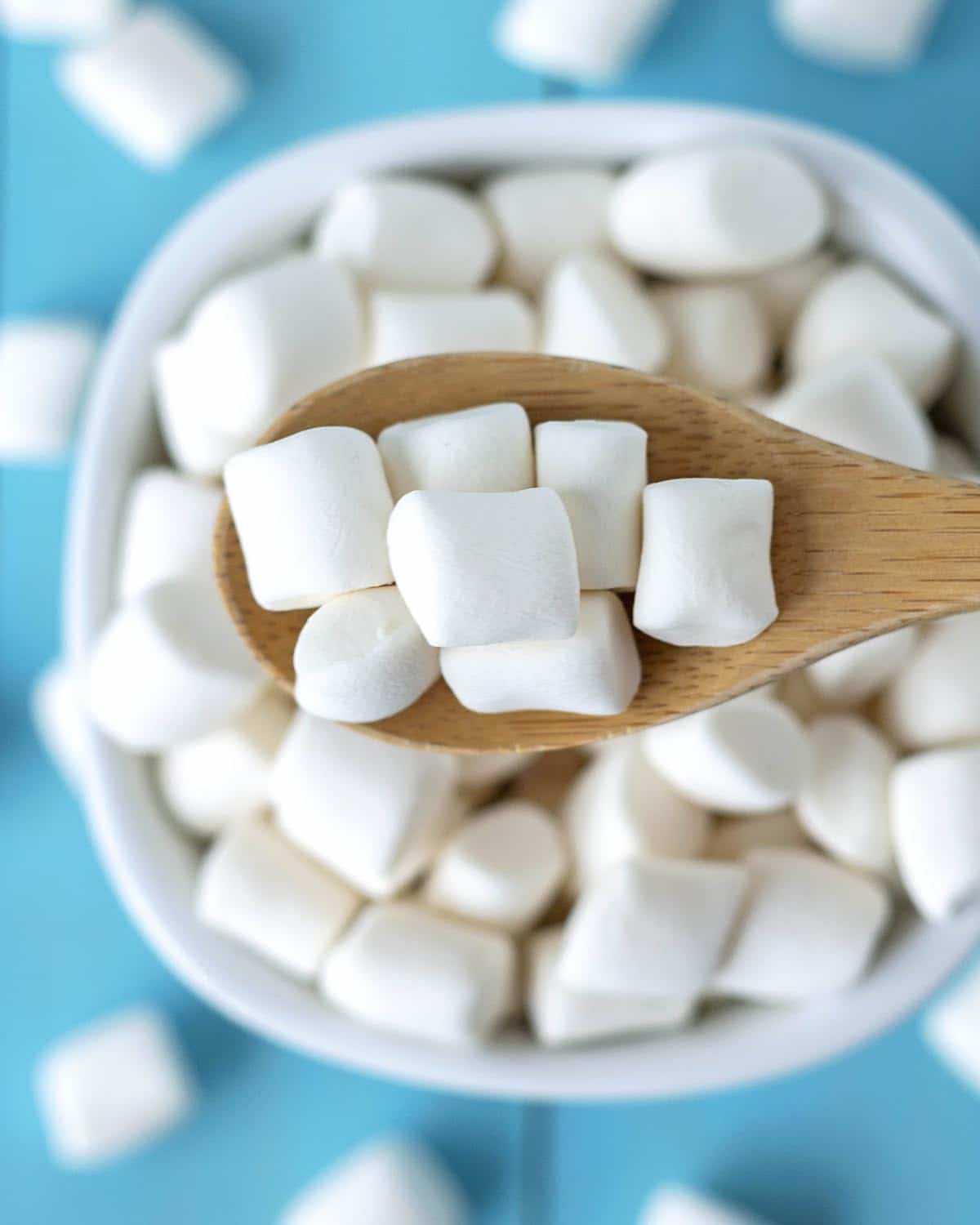 A small wood spoon full of vegan marshmallows being held over a bowl.