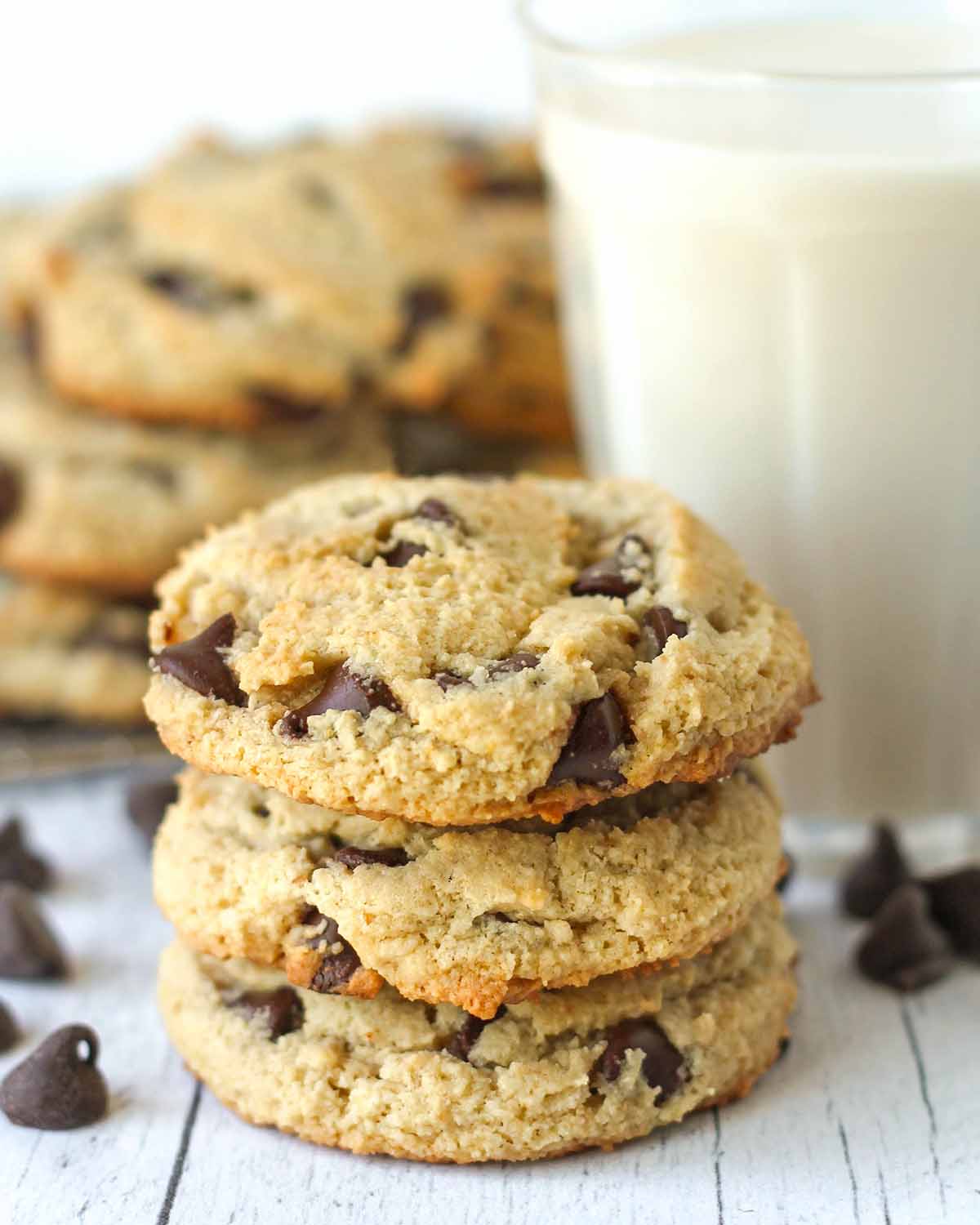 A stack of three vegan almond flour cookies, a glass of almond milk sits behind the cookies.