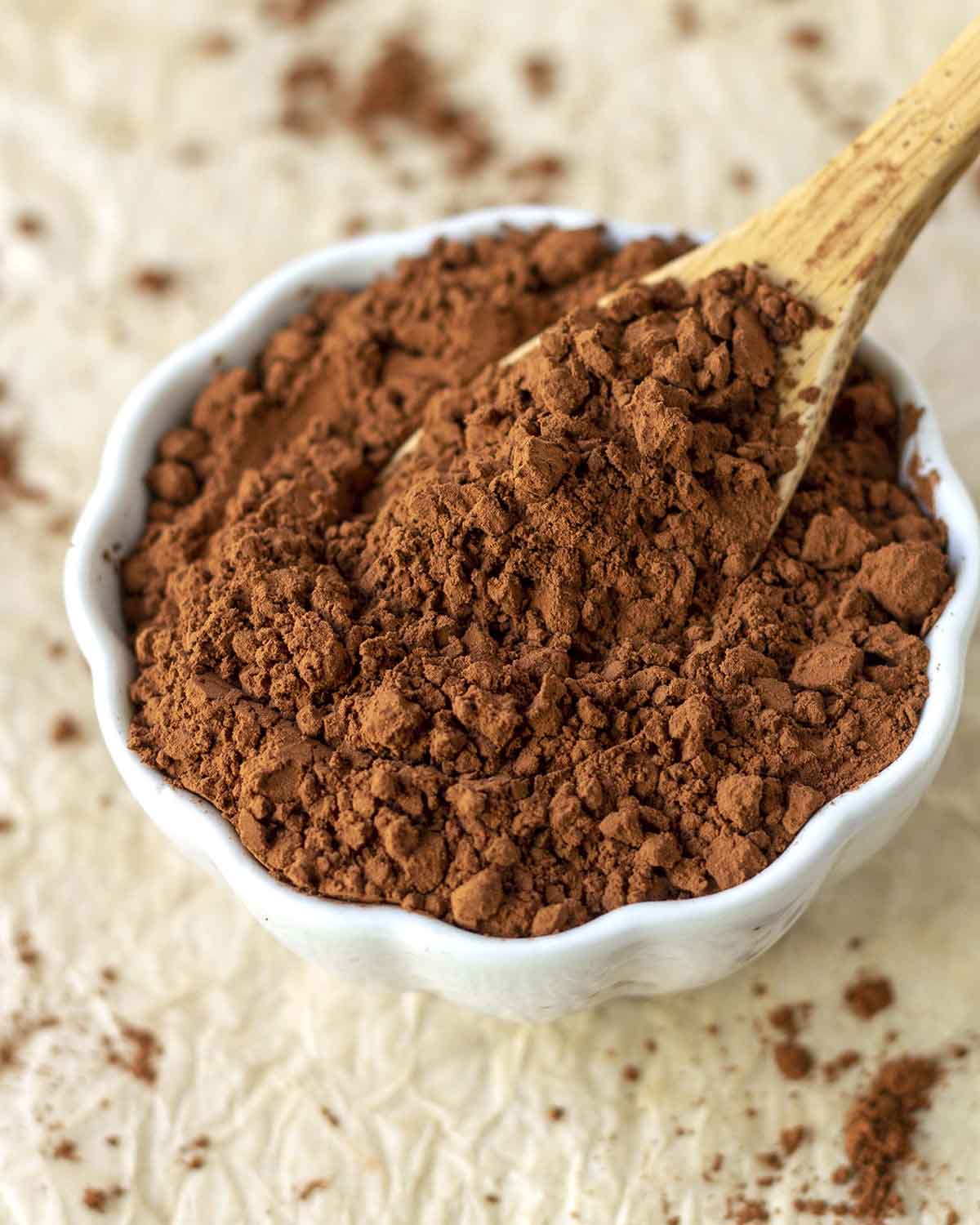 Vegan cocoa powder in a small white bowl, a small wood spoon is in the bowl.