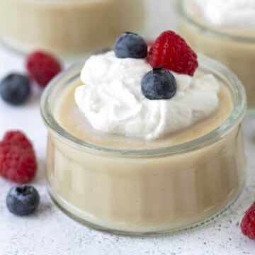A small glass dish filled with vegan gluten-free vanilla pudding, coconut whip and berries.