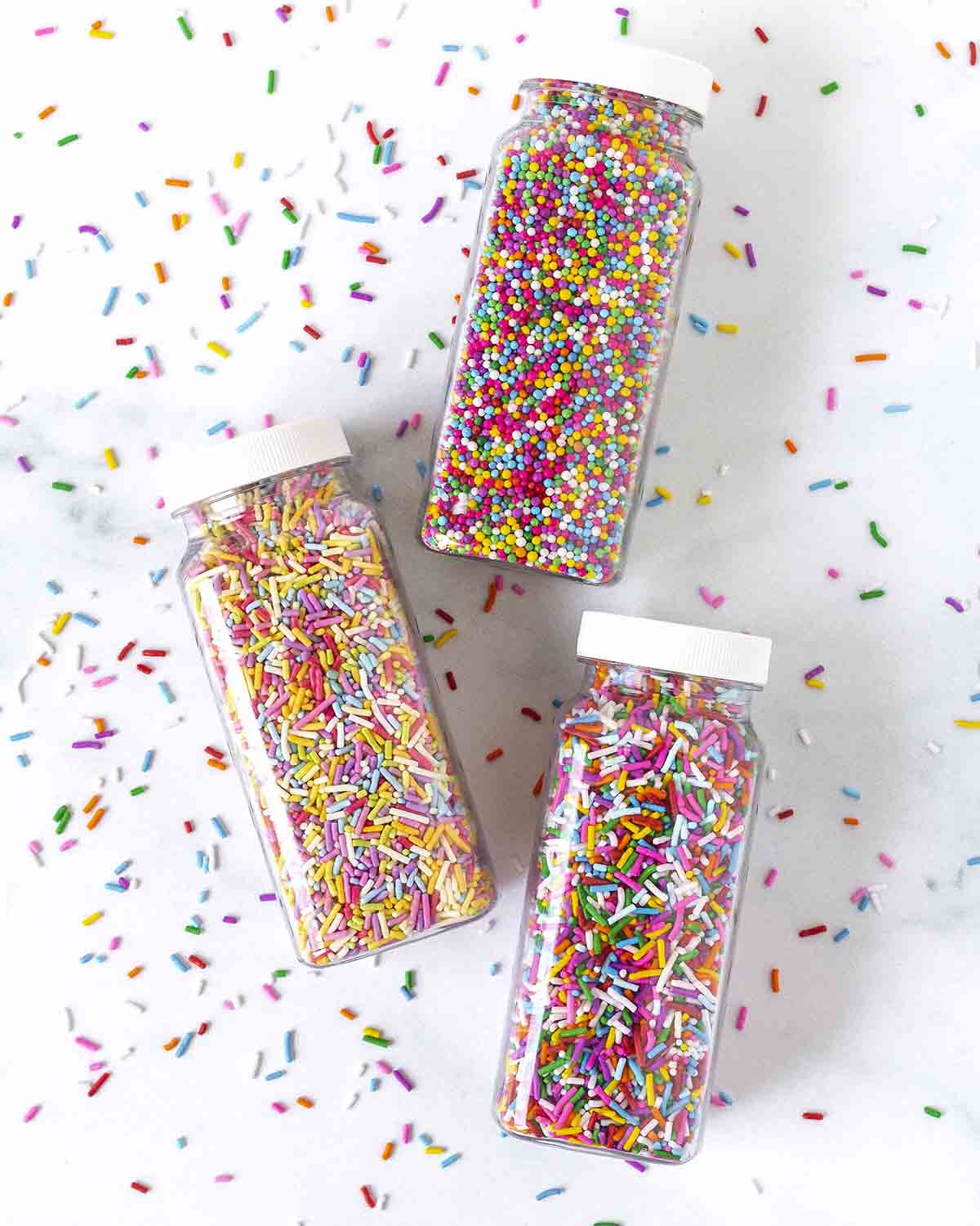 An overhead shot of three jars of gluten-free sprinkles, the jars are on a white table.