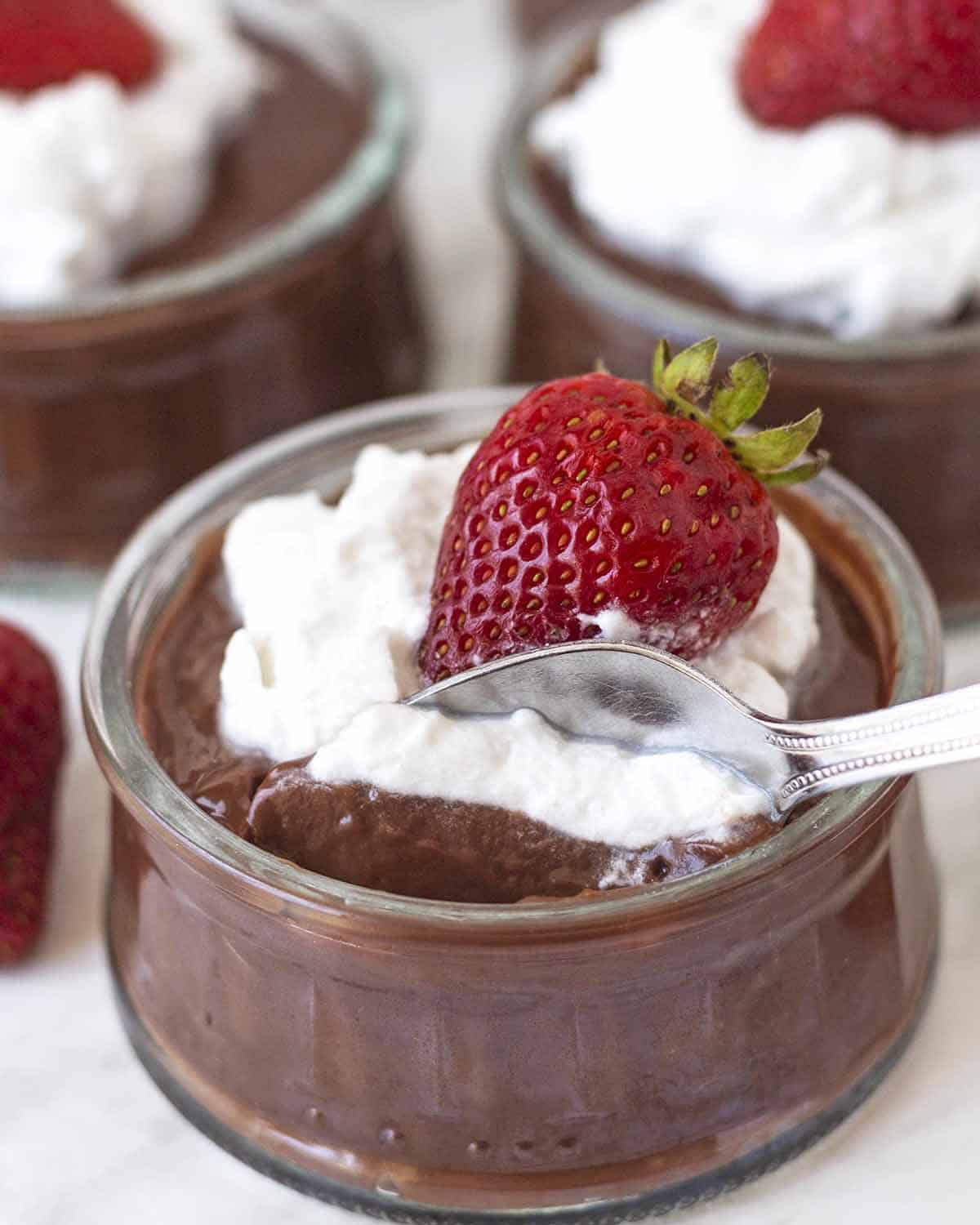 A spoon scooping out a spoonful of chocolate pudding and coconut whipped cream from a small bowl.