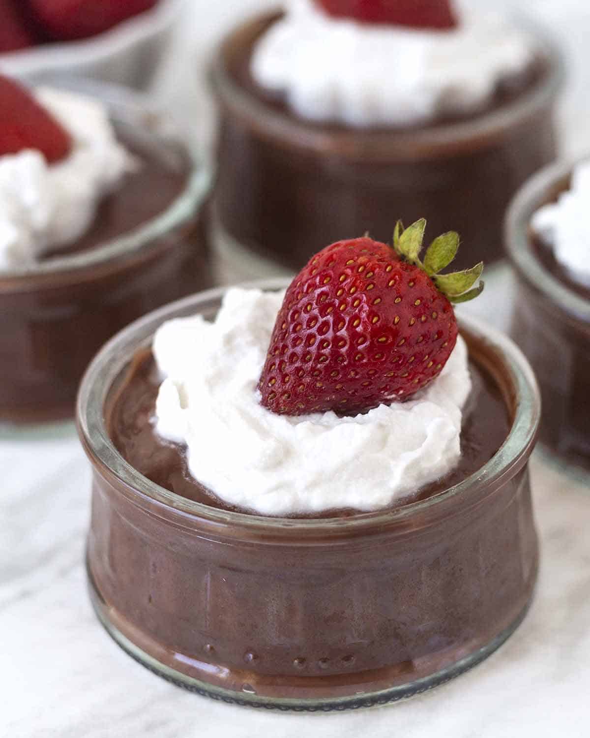 Chocolate pudding in a glass bowl garnished with whipped cream and a fresh strawberry.
