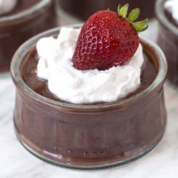 A small glass dish filled with vegan chocolate pudding topped with coconut whip and a fresh strawberry.
