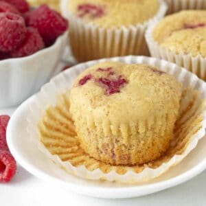 A dairy-free raspberry muffin on a plate with its muffin wrapper peeled down.