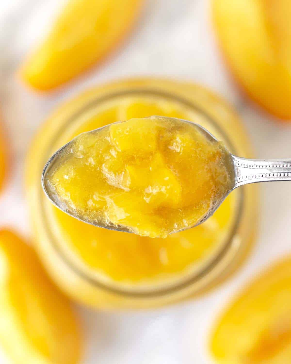 A teaspoon filled with peach sauce; the spoon is being held over a jar of the same sauce.