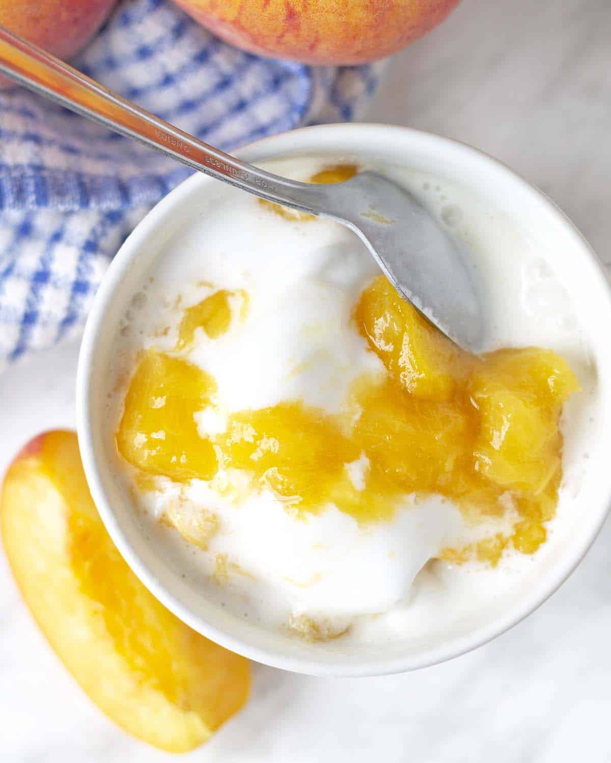 Coconut ice cream in a small bowl with fresh peach sauce swirled into the ice cream, a spoon sits in the bowl.