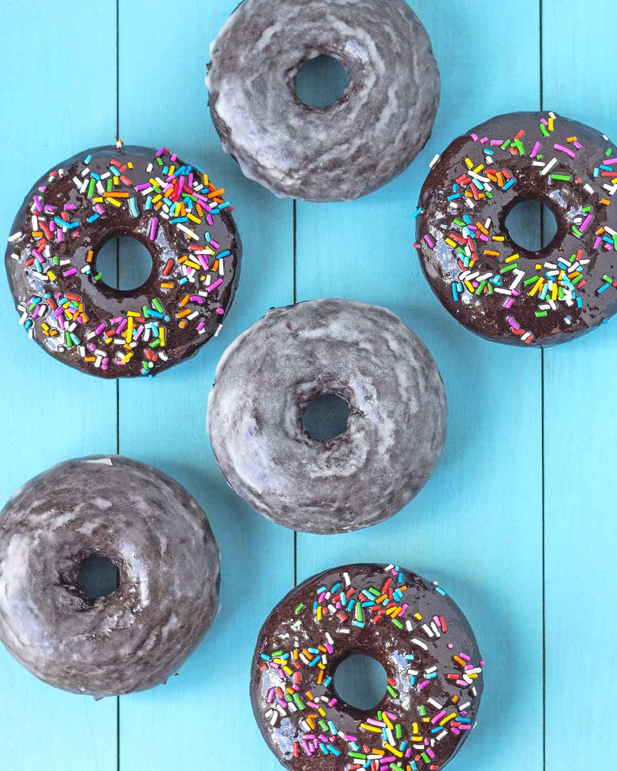 An overhead shot that shows six donuts sitting on a blue wood table.