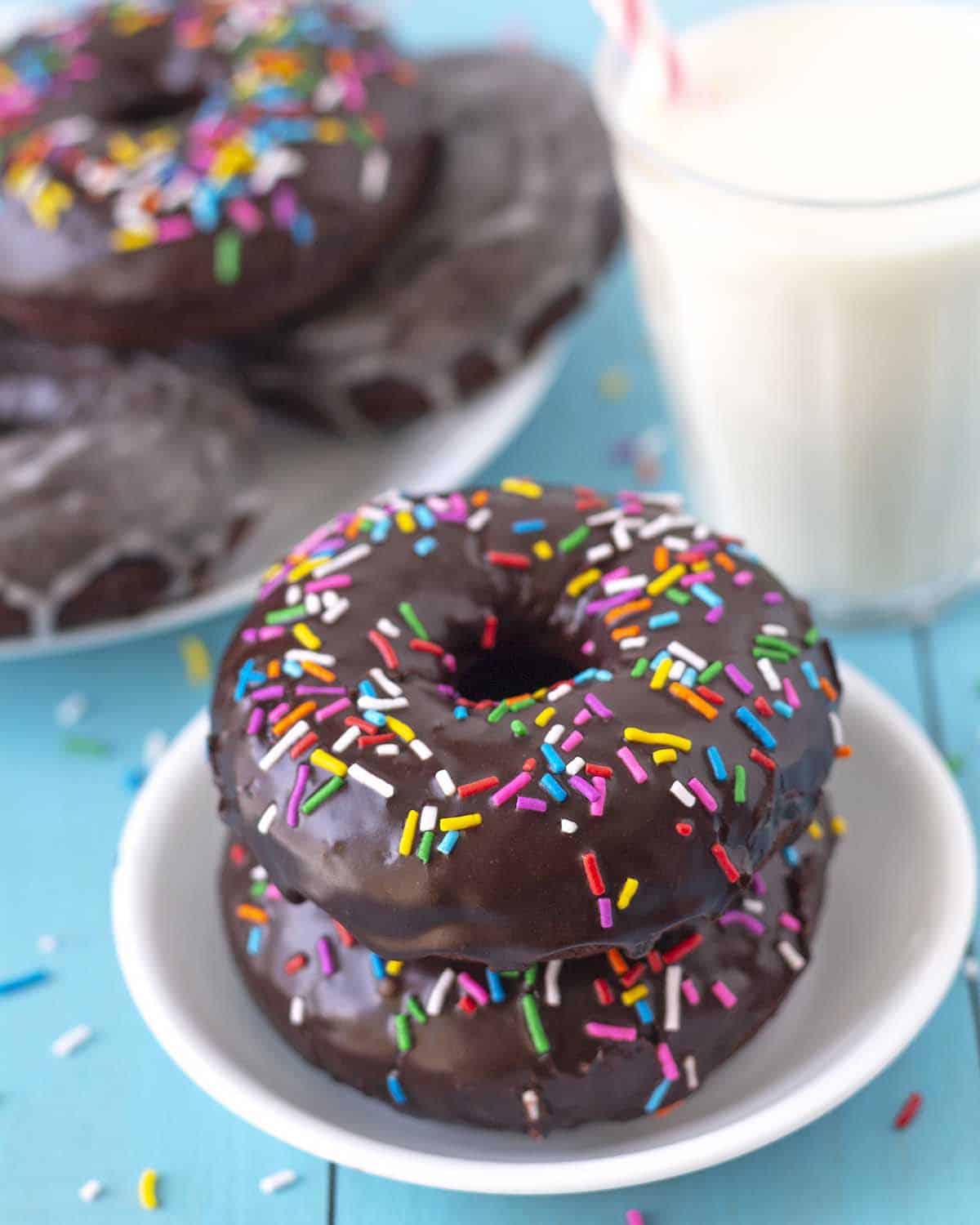 Two chocolate dipped vegan chocolate donuts with sprinkles sitting on a small white plate.