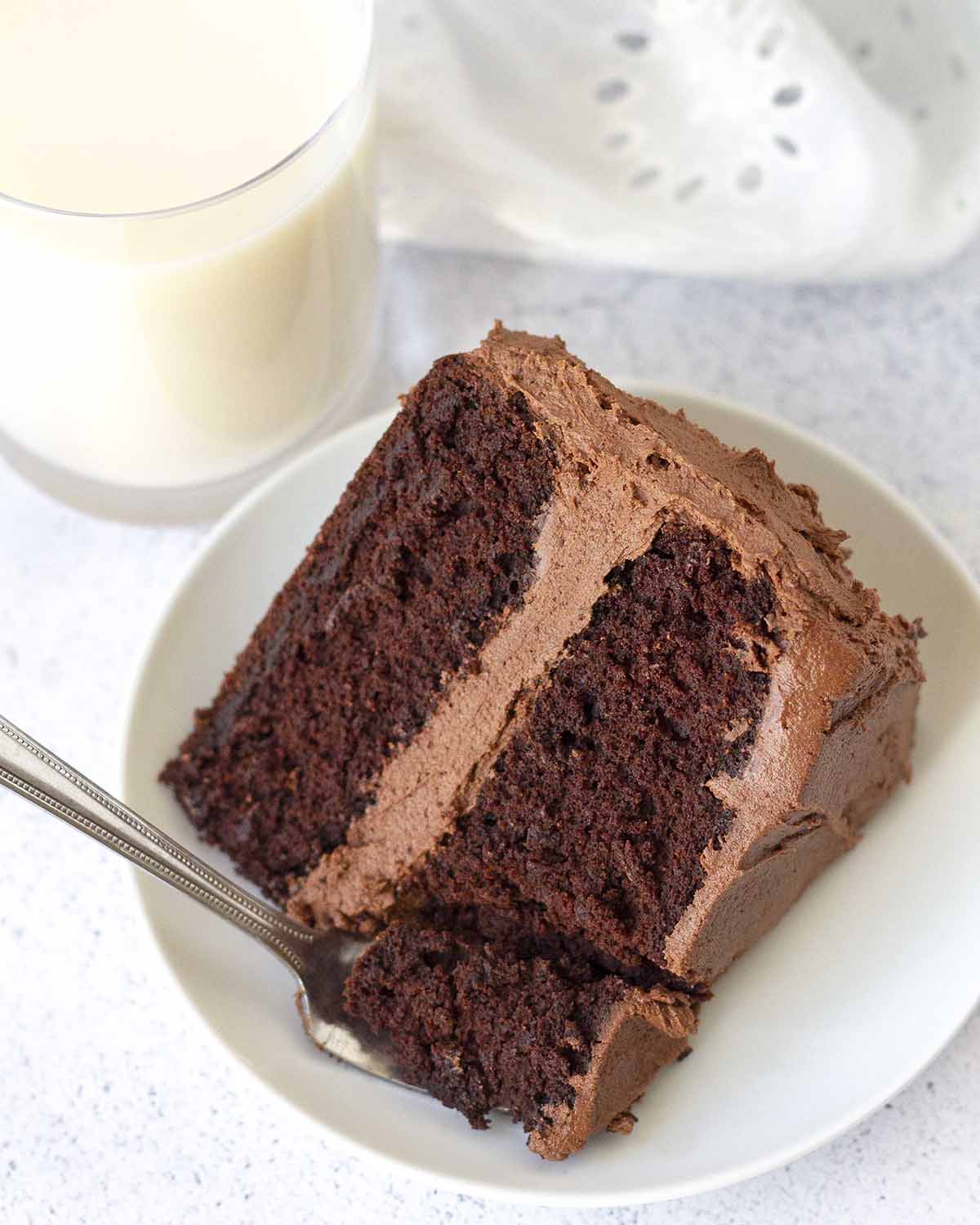 An overhead shot of a slice of chocolate cake, a fork that is resting on the place has taken a piece of the cake.