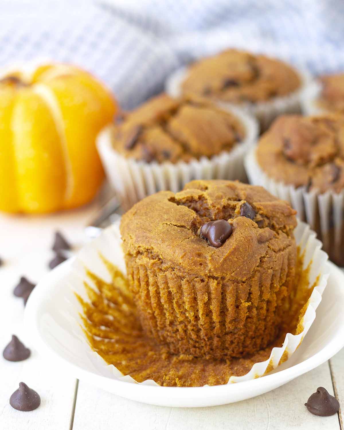 A pumpkin spice muffin on a plate, the muffin wrapper has been peeled away.