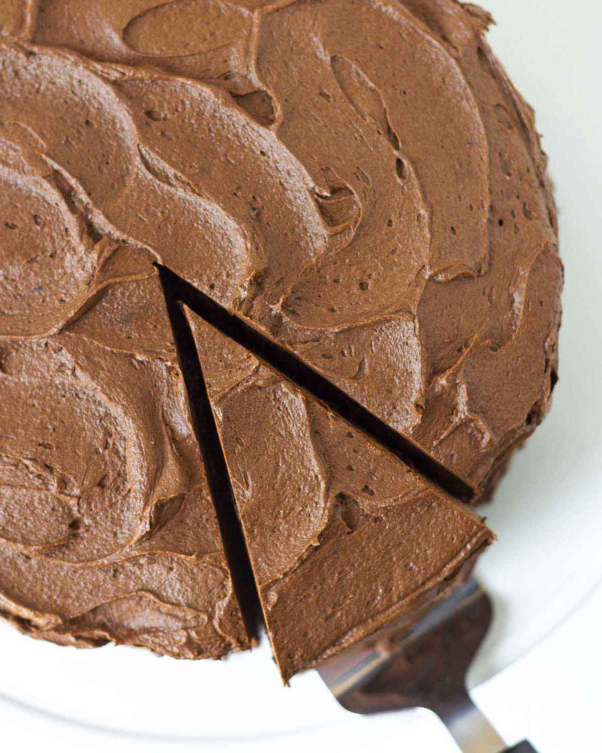 An overhead shot showing a frosted chocolate cake with a slice cut out and being pulled away with a cake server.