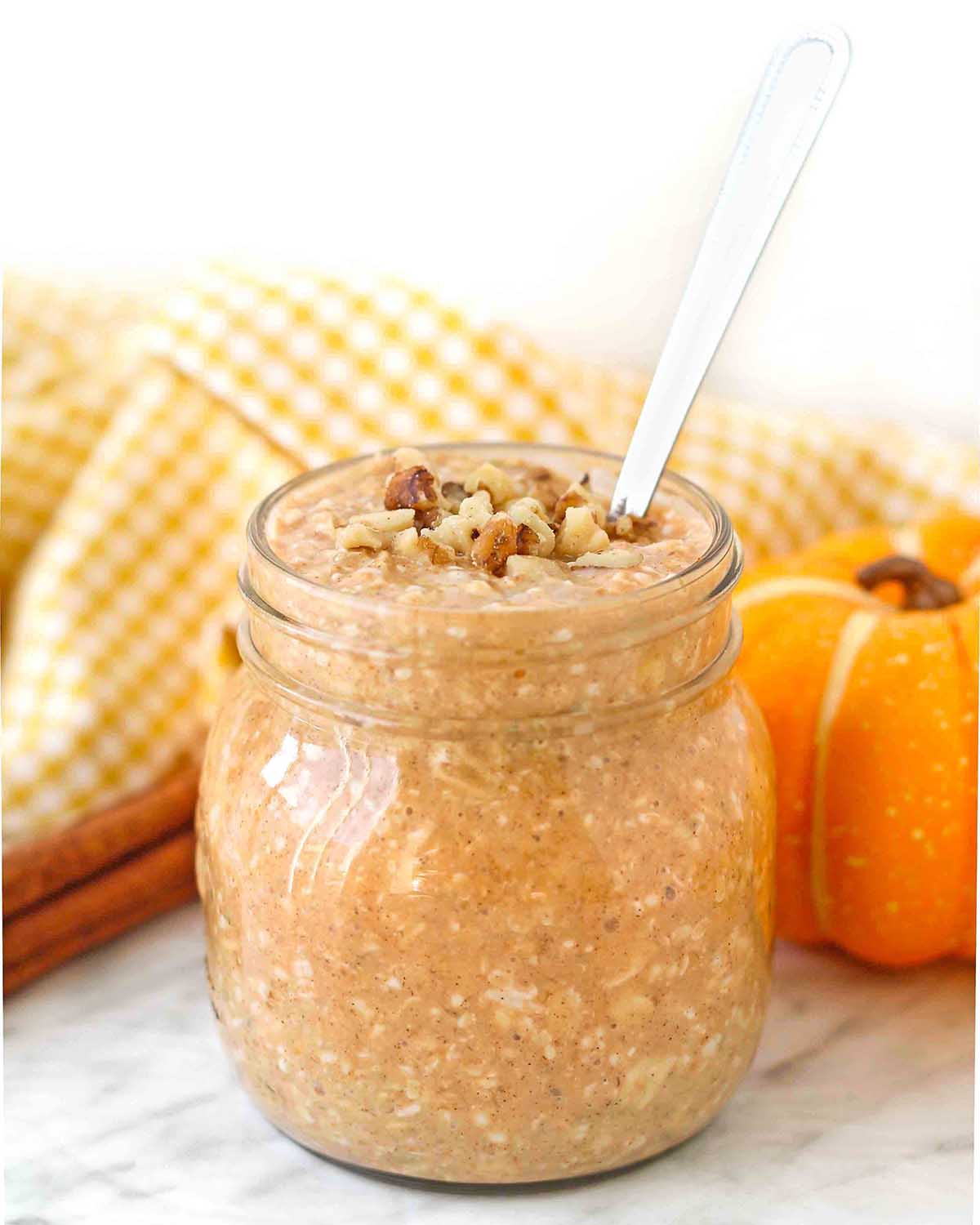 A mason jar of vegan pumpkin overnight oats topped with walnuts; a spoon is in the jar.