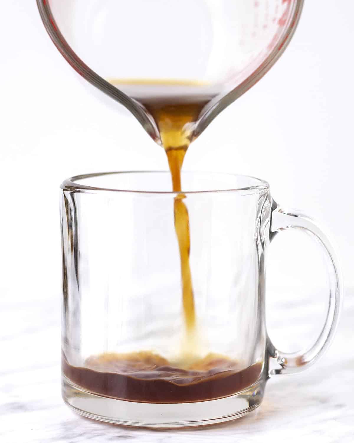 Freshly brewed coffee being poured into a clear glass mug.