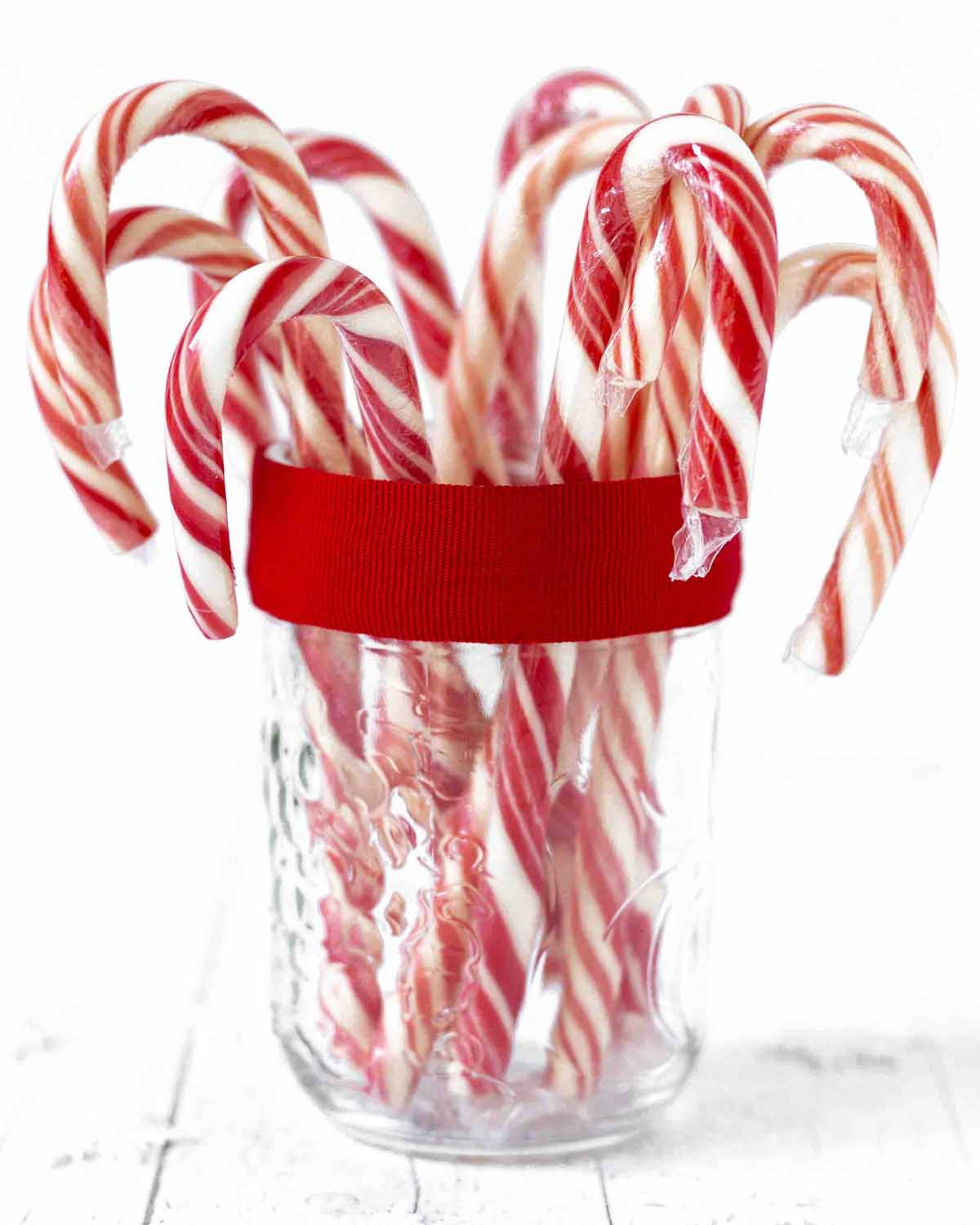 A glass mason jar with candy canes inside of it.