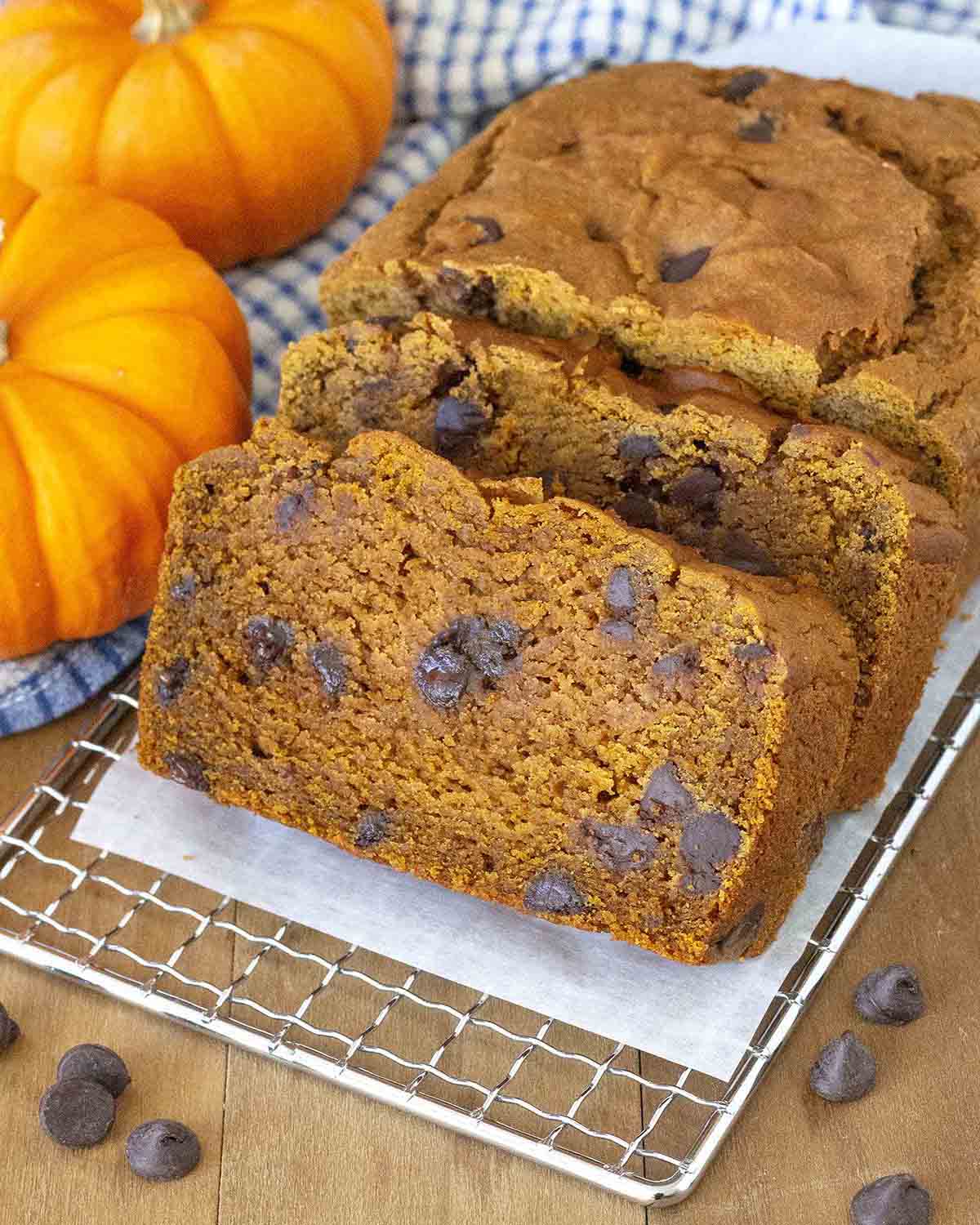 A loaf of pumpkin bread on a small cooling rack, two pieces have been sliced and sit in front of the loaf.