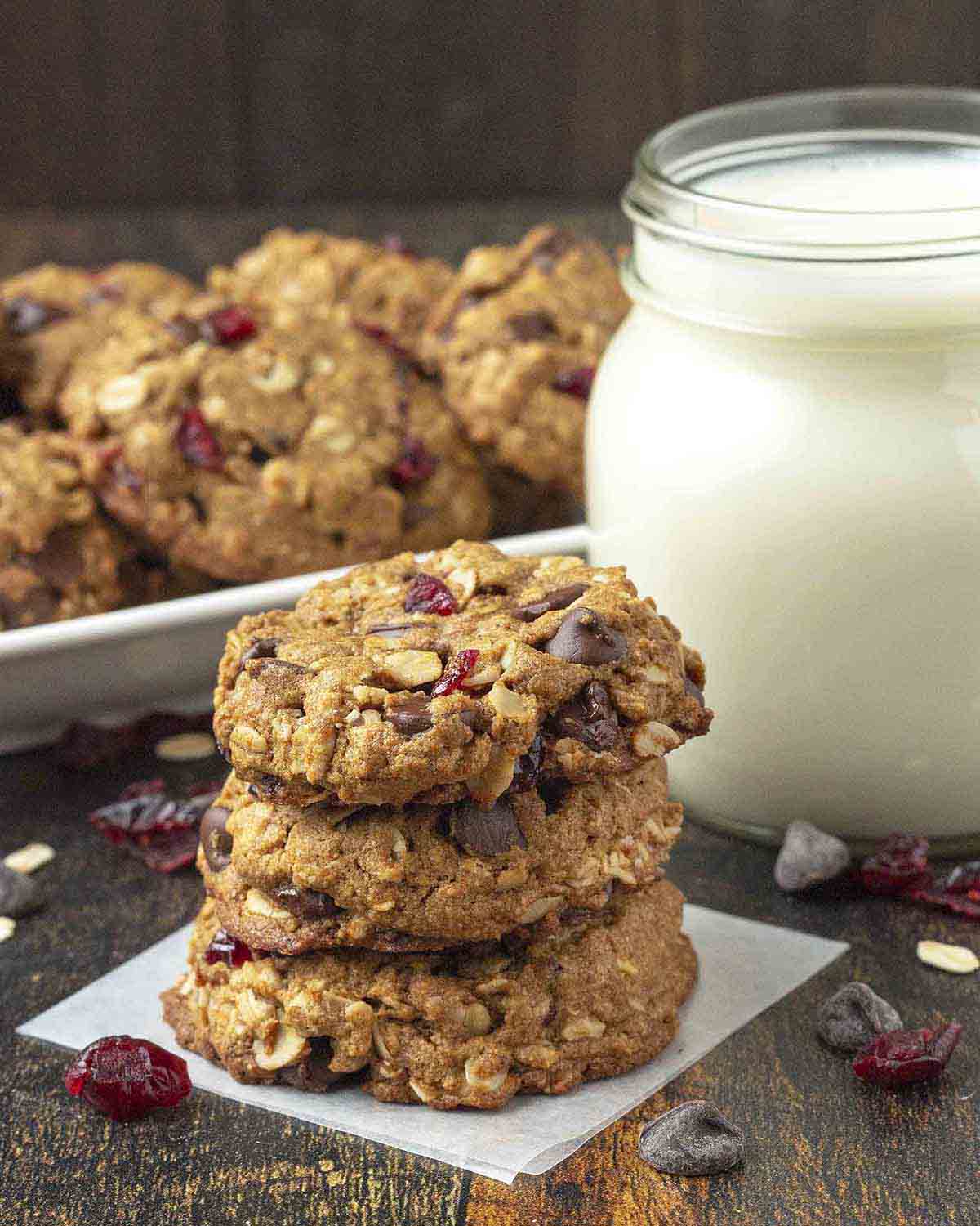 A stack of three vegan oatmeal cranberry chocolate chip cookies sitting on a dark wood table.