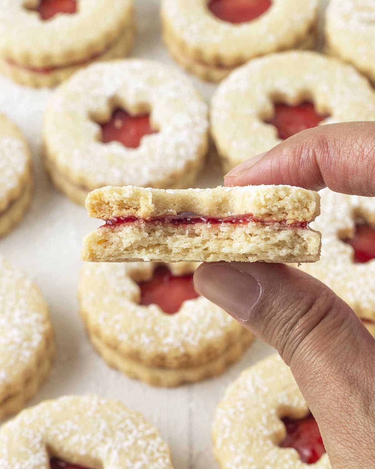A hand holding up a Linzer cookie broken in half to show the inner crunchy texture.