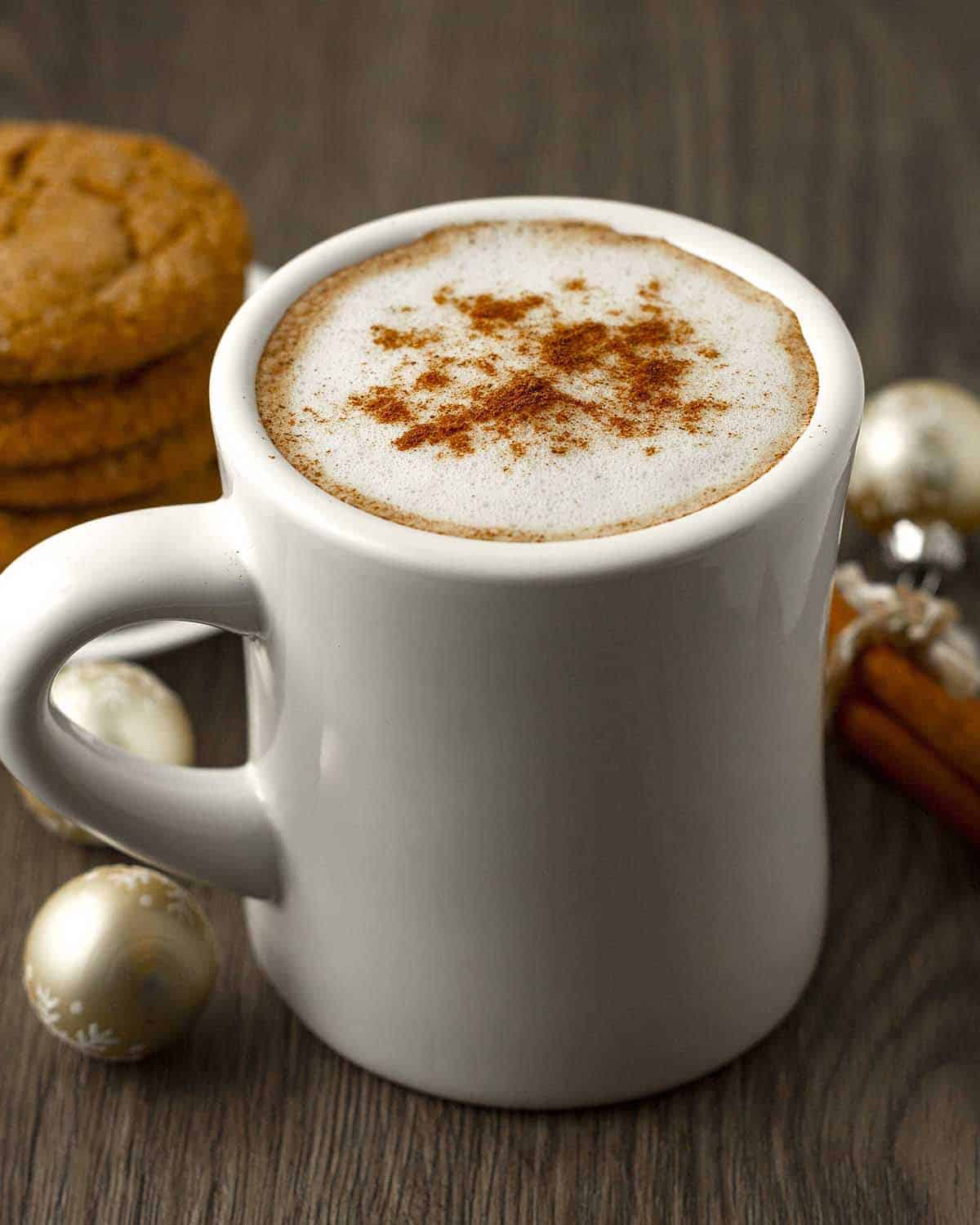 A mug filled with gingerbread latte, the drink is topped with foamed milk and a dusting of ground cinnamon.