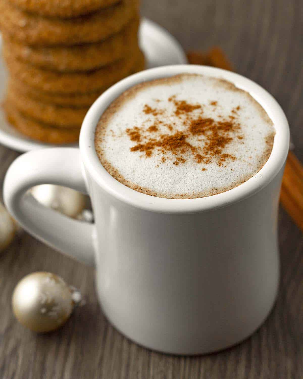 An overhead shot showing a homemade gingerbread latte in a white mug, gingerbread cookies sit behind the mug.