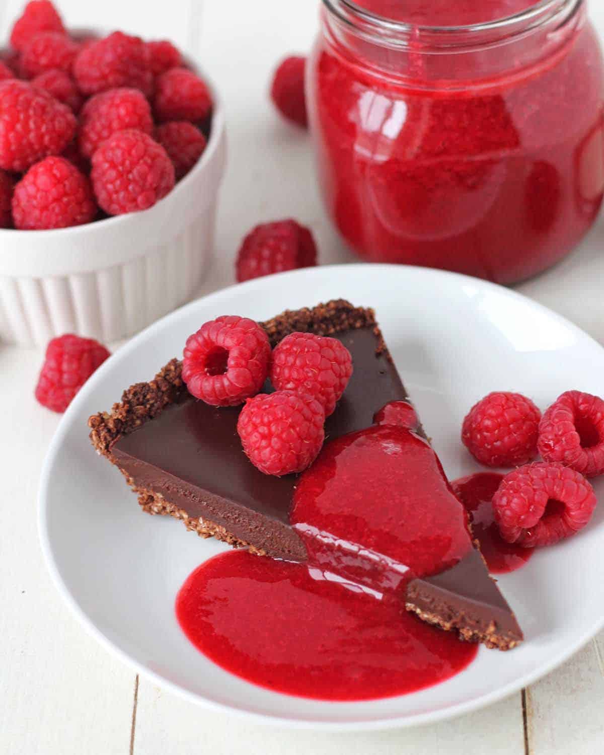 A slice of chocolate tart garnished with raspberry sauce on a white plate.