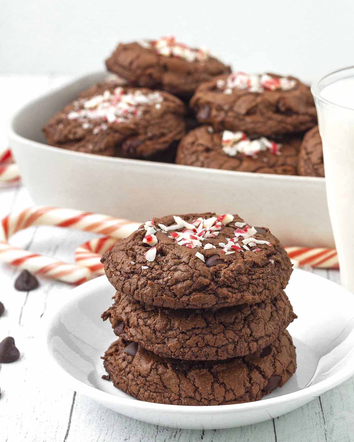 Chocolate peppermint cookies on a small white plate, more cookies sit behind the plate in a serving dish.