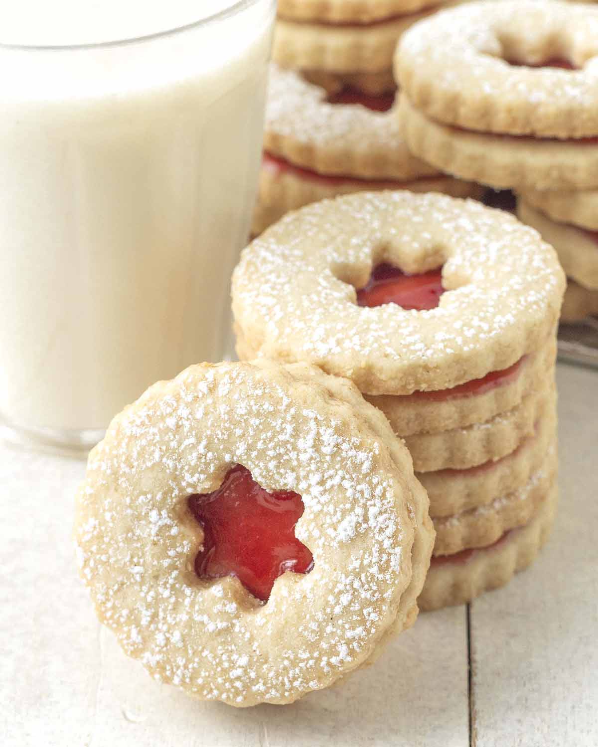A stack of Linzer cookies with one cookie leaning against the stack, more cookies sit in the background.
