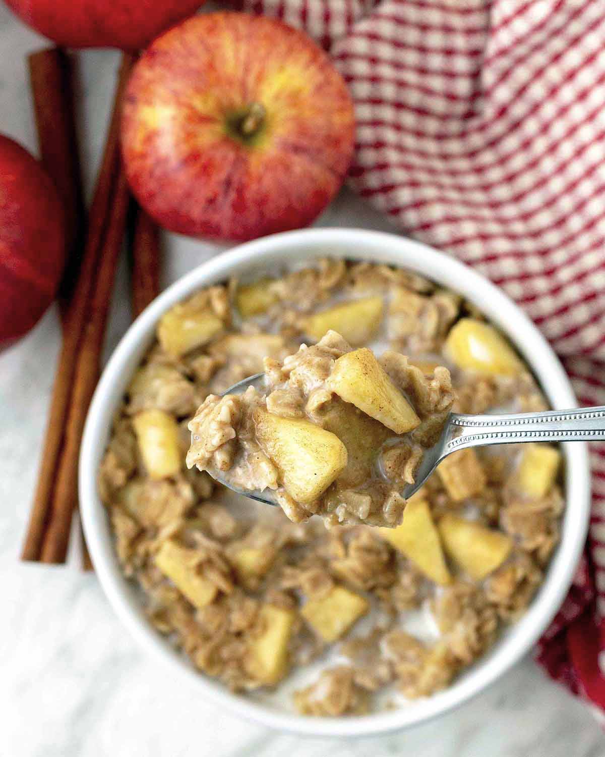 A spoonful of vegan apple cinnamon oatmeal being held up above a full bowl of the same oatmeal.
