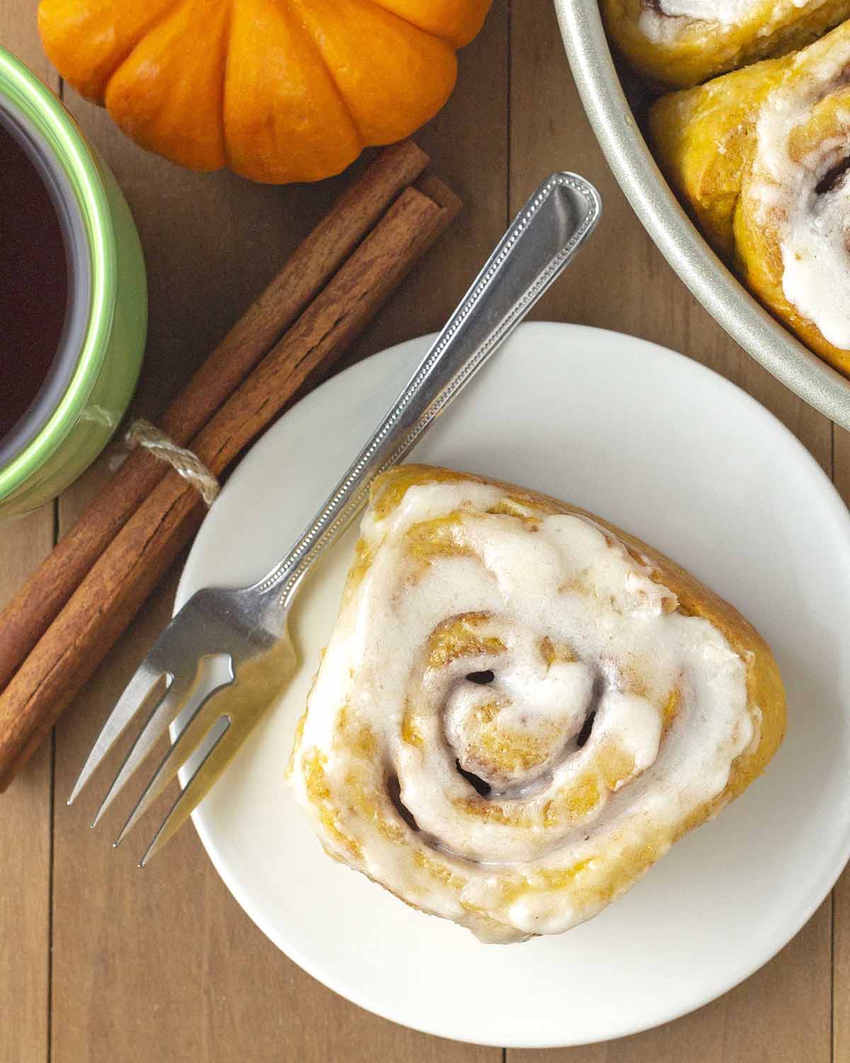 Overhead images showing a frosted pumpkin cinnamon roll on a white plate.
