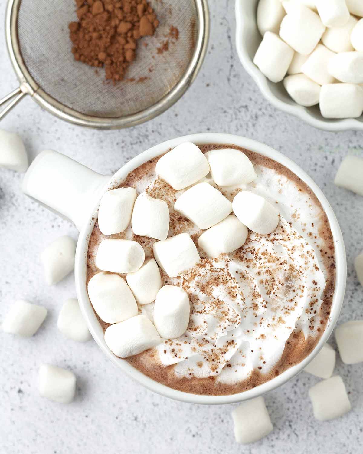 An overhead shot of vegan hot chocolate in a mug and garnished with marshmallows and coconut whip.