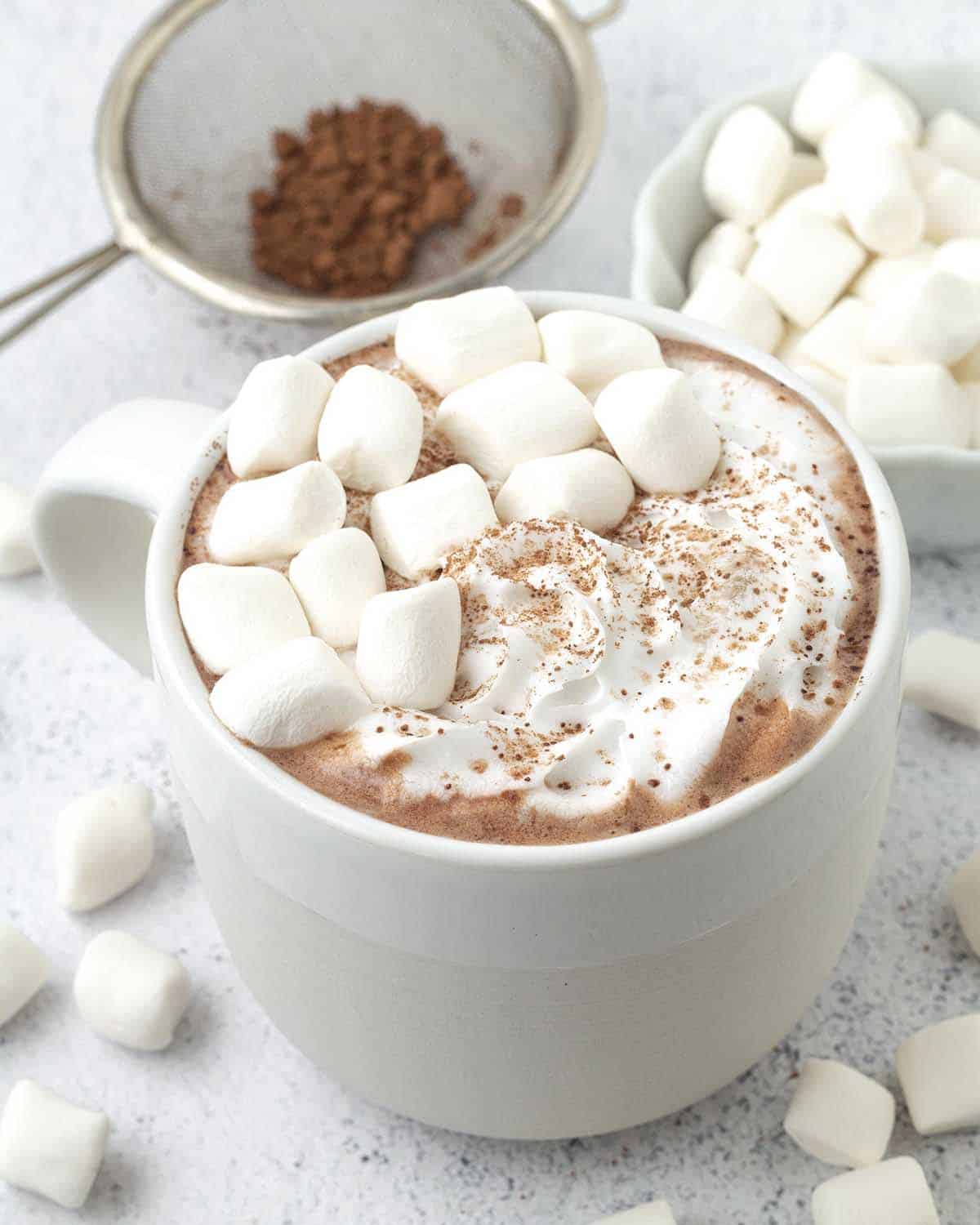 A mug of vegan hot cocoa garnished with mini marshmallows and vegan whipped cream.