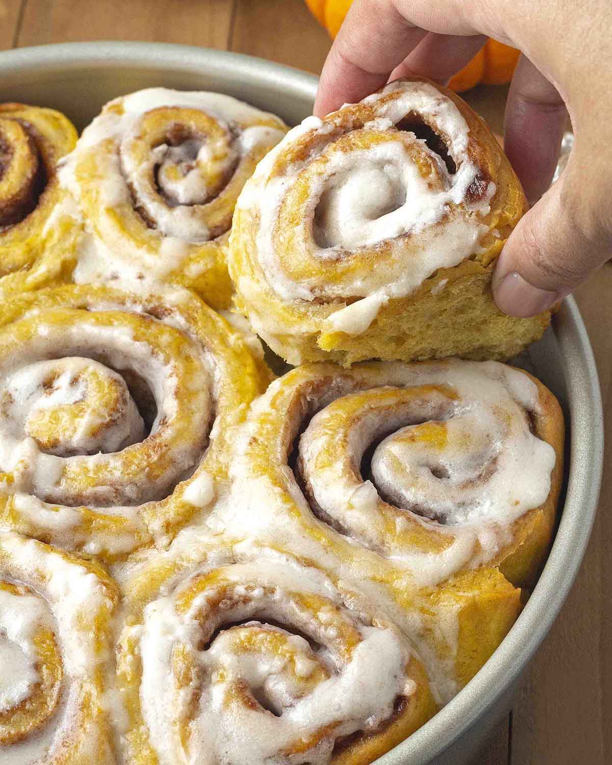 A hand taking a freshly baked pumpkin cinnamon roll out of the pan.