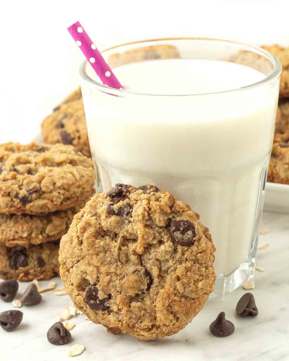 An almond flour oatmeal cookie leaning against a glass of almond milk.