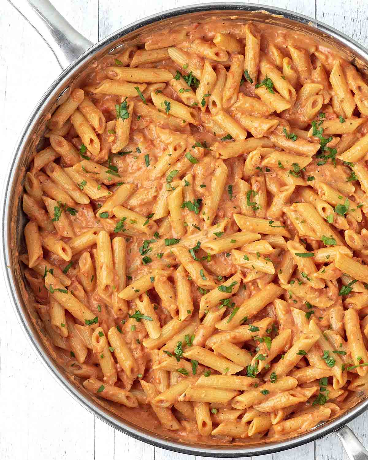 An overhead image of freshly made dairy-free tomato pasta garnished with chopped parsley in a large pan.