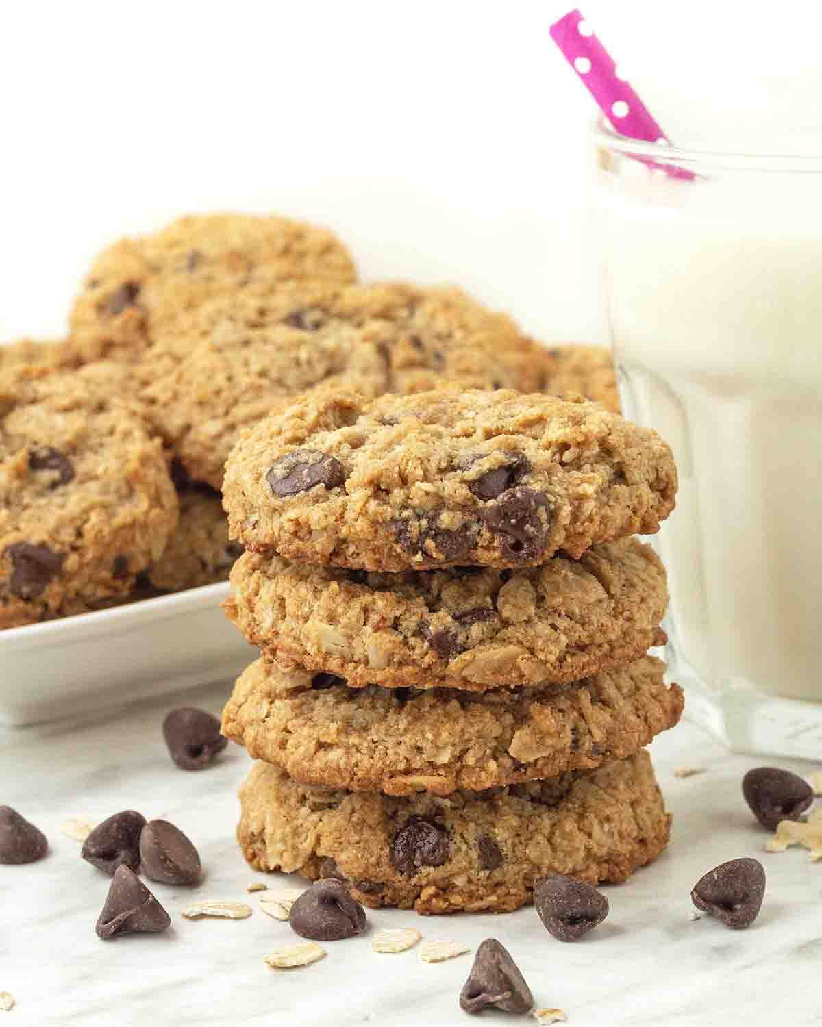 A stack of four vegan almond flour oatmeal chocolate chip cookies on a table, more cookies sit behind them.