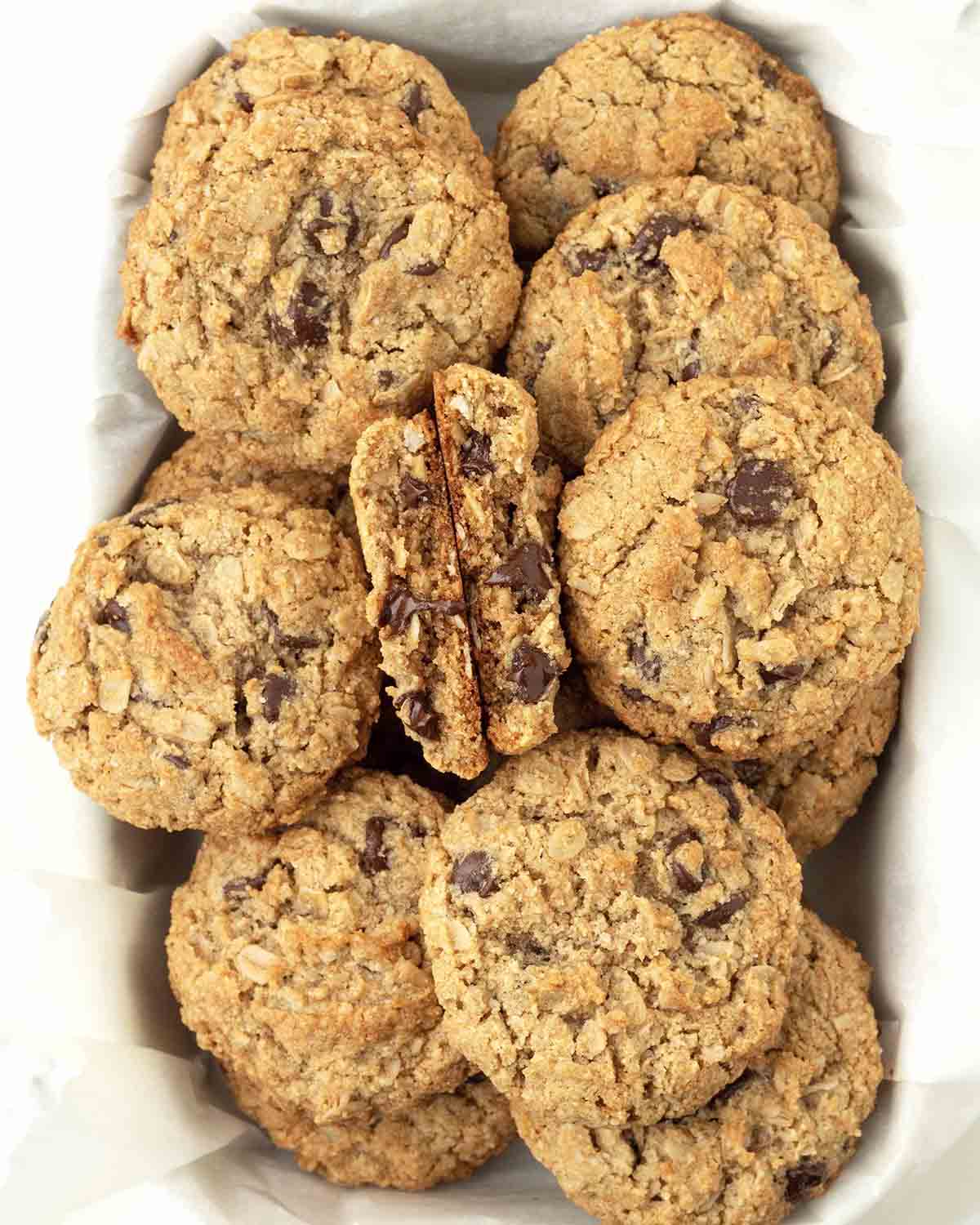 An overhead shot of vegan almond flour oatmeal cookies in a serving dish, one cookie is split in half to show the inside.