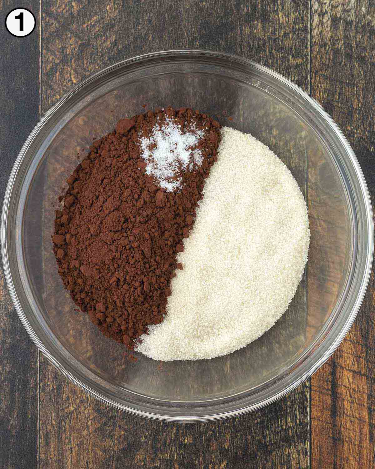 The three ingredients for hot cocoa mix in a glass bowl with a whisk.