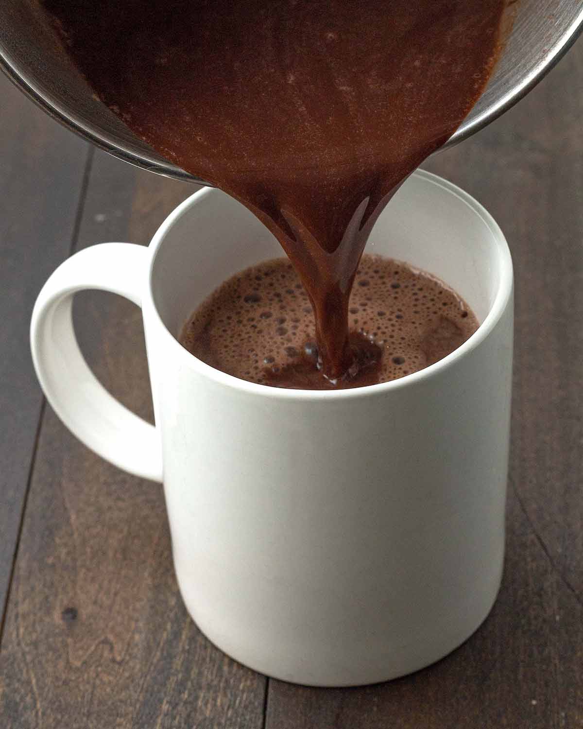 Homemade peppermint hot chocolate being poured from a pot into a white mug.