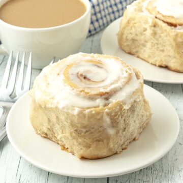 A close up shot of a cinnamon roll sitting on a small white plate beside a fork.