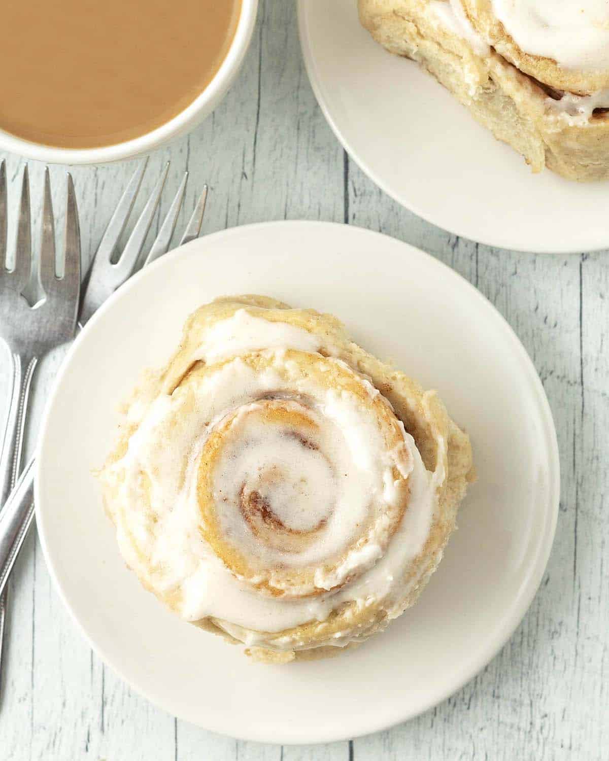 Overhead image showing a frosted cinnamon roll on a white plate.