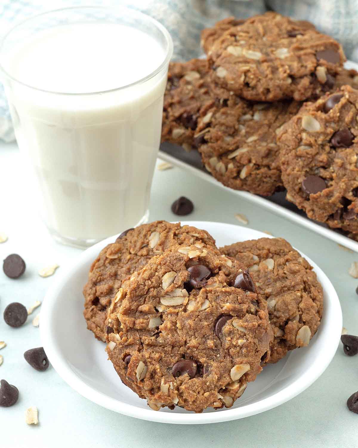 Eggless peanut butter oatmeal cookies on a plate, a glass of almond milk and more cookies sit behind the plate.