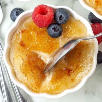 An overhead image of vegan crème brulee, a spoon is cracking the caramelized sugar shell.