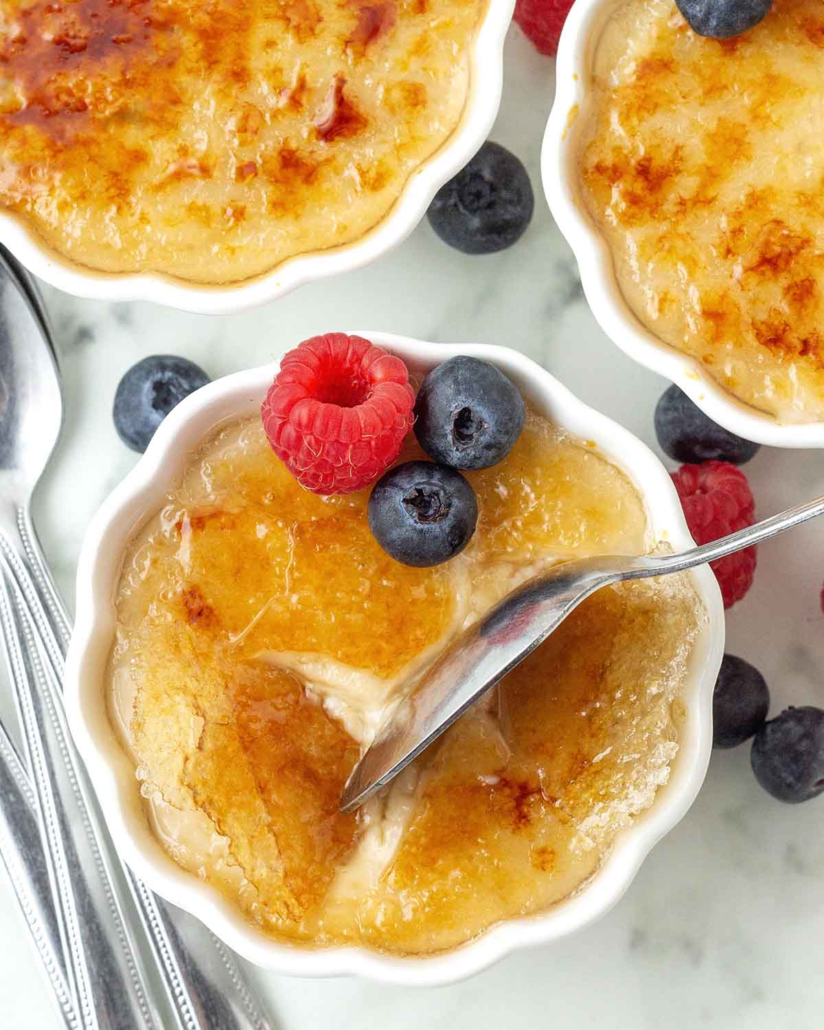 An overhead image of dairy-free crème brulee, a spoon is cracking the golden caramelized sugar shell.