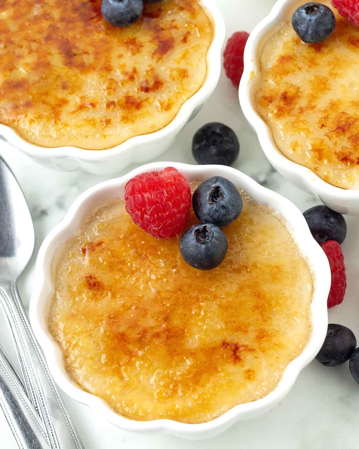 Three ramekins holding vegan crème brulee, the sugar has been caramelized and there are fresh berries on top for garnish.